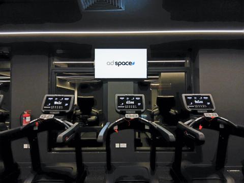 An Ad Space screen above a row of treadmills in a gym