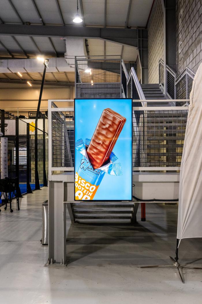 A tall Ad Space screen showing a chocolate ad beside the courts, at a padel club in Kuwait