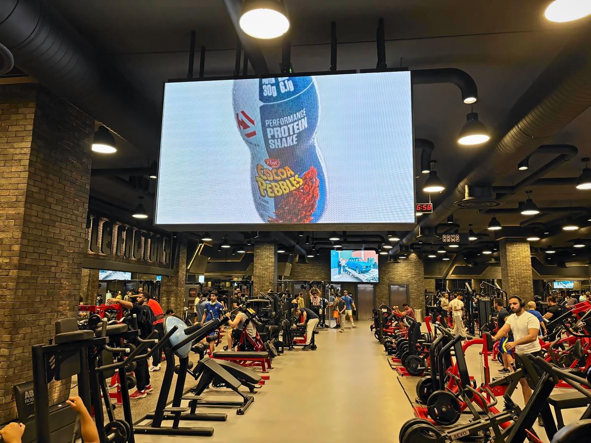 A protein shake ad on a giant Ad Space screen over a packed gym floor in Kuwait